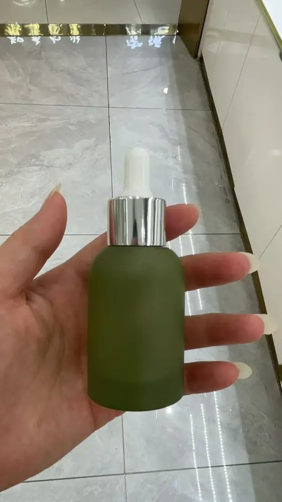 Chai thủy tinh phun mờ màu xanh rêu cầm trên tay